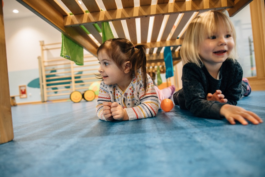 Zwei kleine Kinder lächeln und verstecken sich unter einer Holzbank.