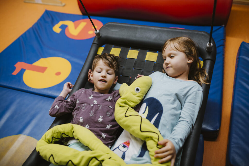 Zwei Kinder liegen in einer Hängematte. In seinen Händen liegt eine große Stofftier Python.