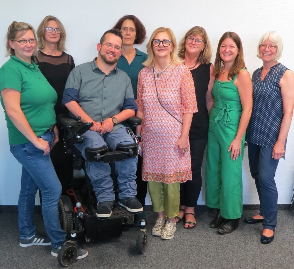 Mehrere Personen nebeneinander. Eine davon im Rollstuhl