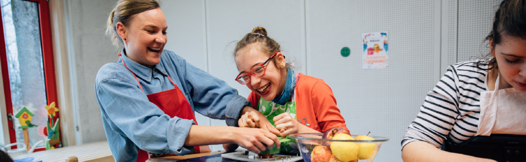 Lachendes Mädchen schneidet Obst mit Hilfe einer Konduktorin