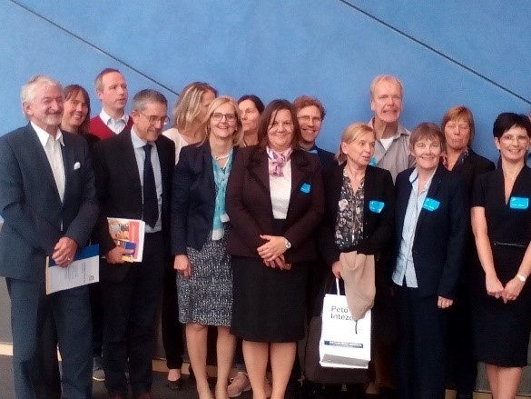 Viele Personen in Anzügen mit blauem Aufkleber am Revers lächeln in die Kamera