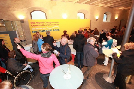 Vielen Personen in einem Raum mit Wandplakat 8th World Congress on Conductive Education Rythm and Balance