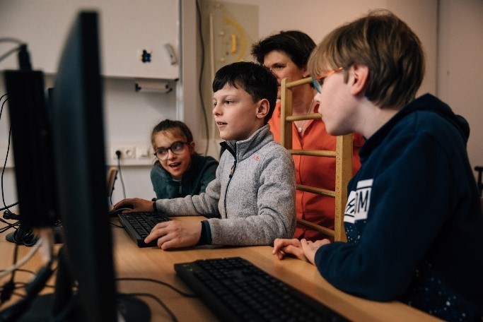 Foto: drei Kinder sitzen am Computer. 