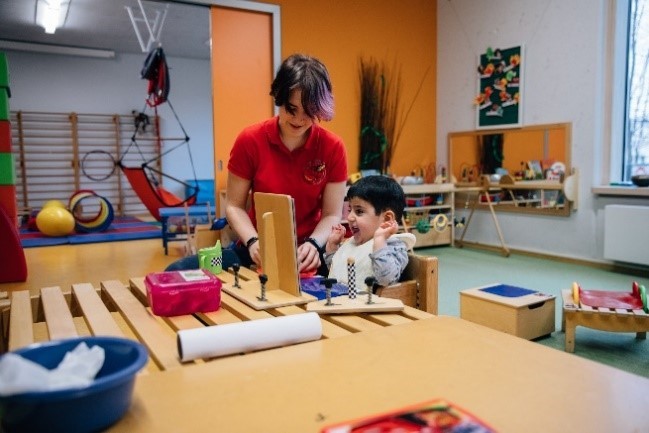 Foto: Ein Junge sitz vor einem Spiegel und macht Übungen mit einem Therapeuten.