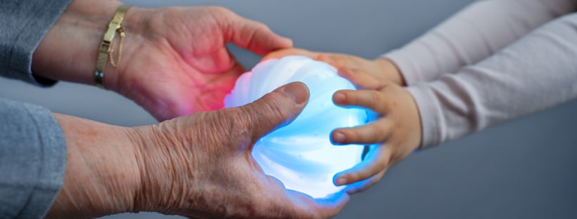 Ältere und sehr junge Person halten einen leuchtenden Ball